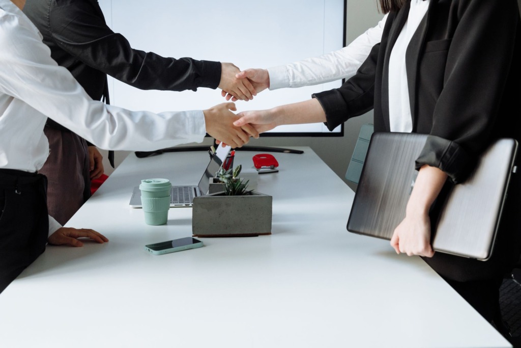 Business partners shaking hands over a meeting table with laptops in a modern boardroom