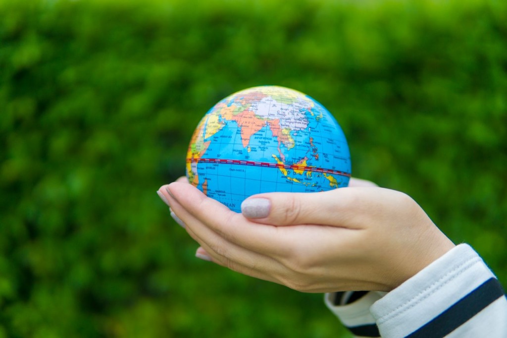 Hands holding a small world globe against a lush green background representing SAAQi Tech expanding globally from Pakistan