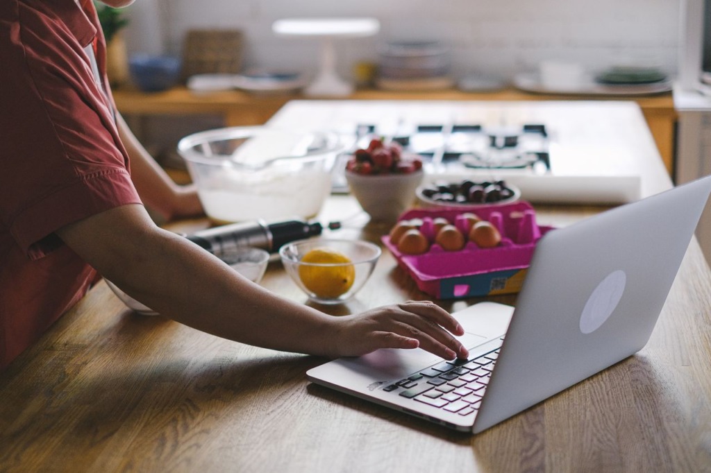 Fresh ingredients, bowls, and baking equipment arranged around an open laptop on a kitchen counter