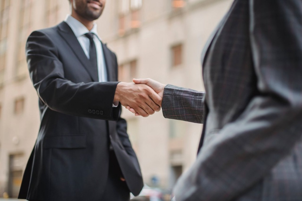 Two business professionals in dark suits shaking hands inside a modern office space