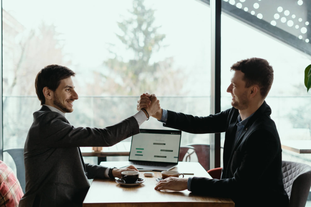 Two businessmen shaking hands across a conference table in a modern bright office
