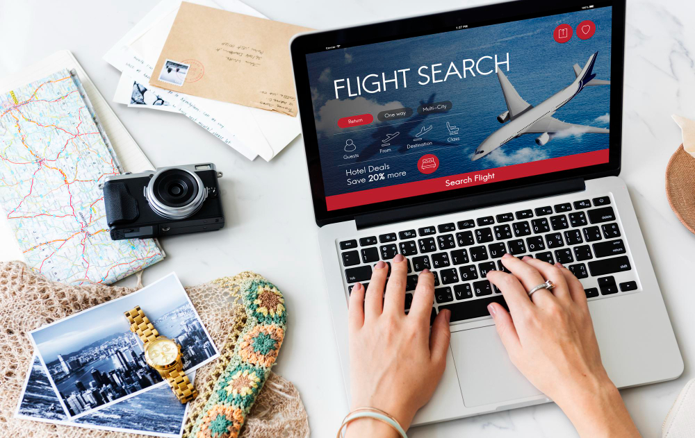 Overhead view of hands searching for flight bookings on a laptop screen with travel maps nearby