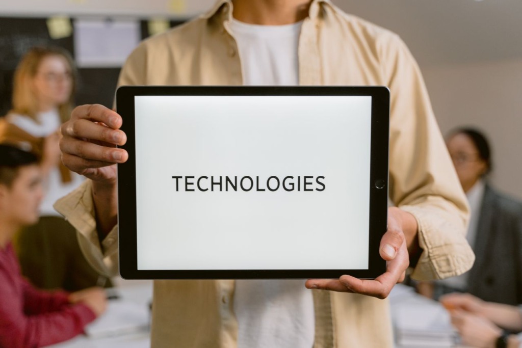 Person holding up a digital tablet displaying the word TECHNOLOGIES on a clean white screen